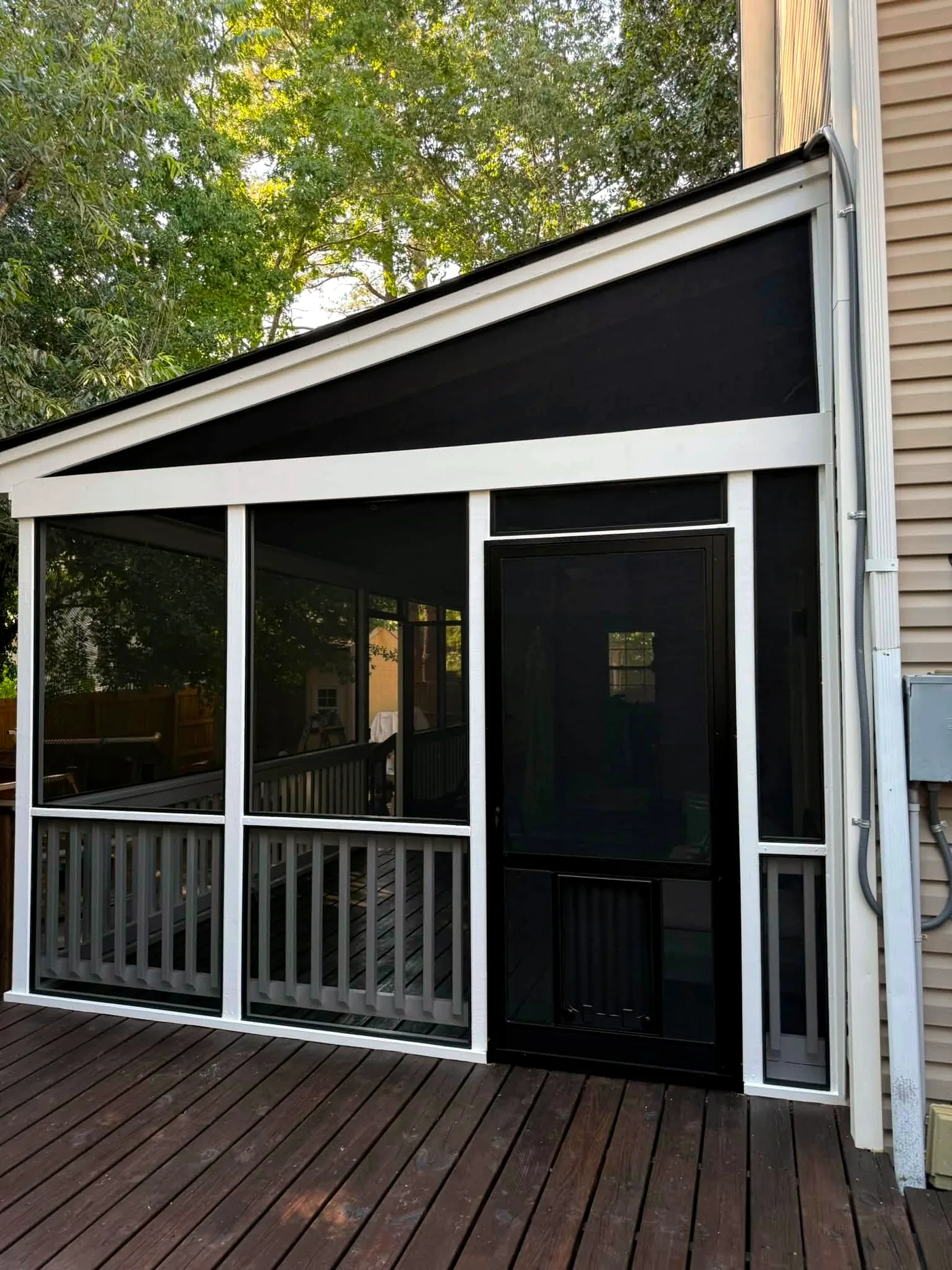 Black screen door with a built-in pet door on a white-framed screened deck
