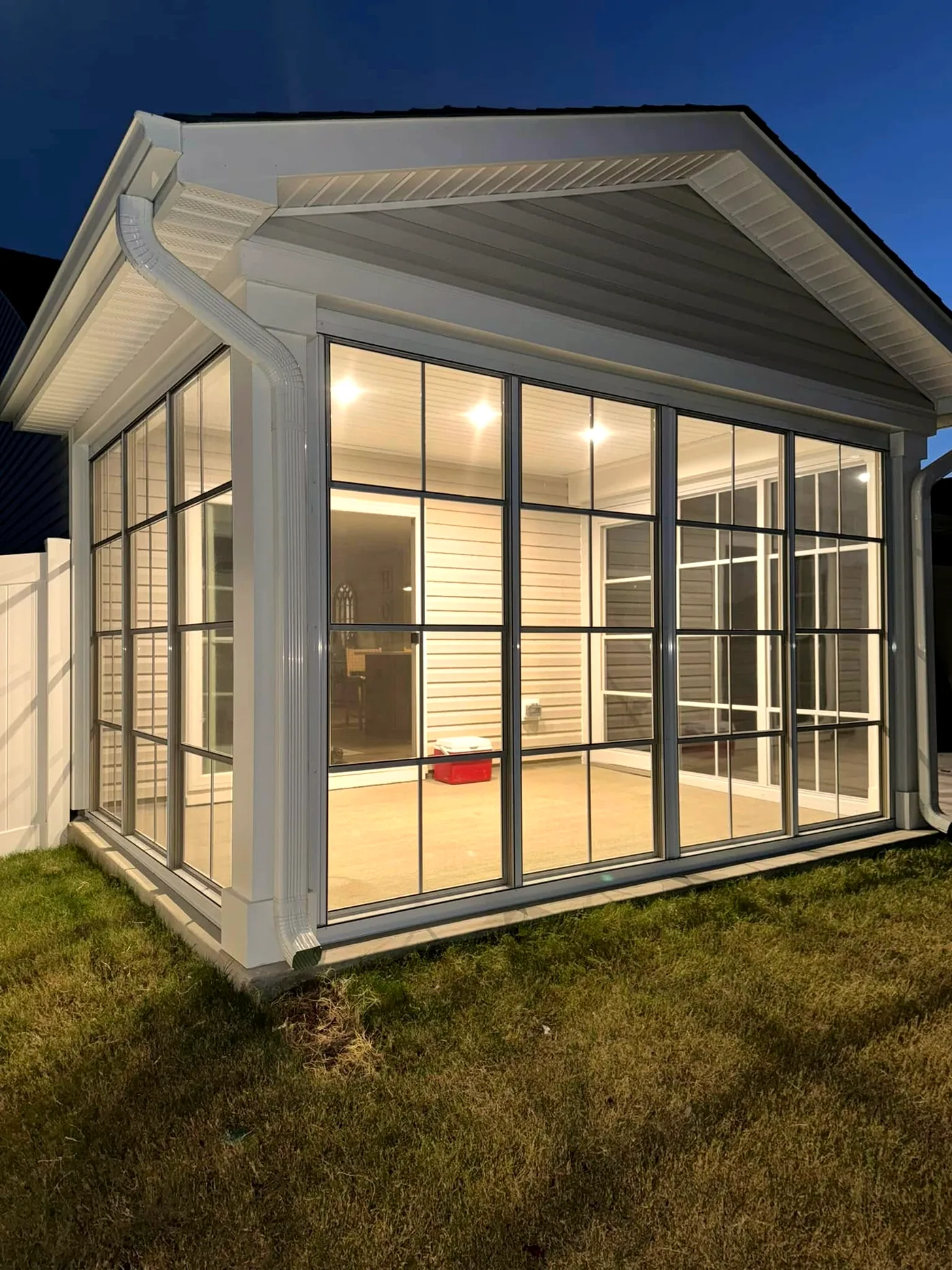 Three-season room with black-grid vinyl windows lit from inside at dusk