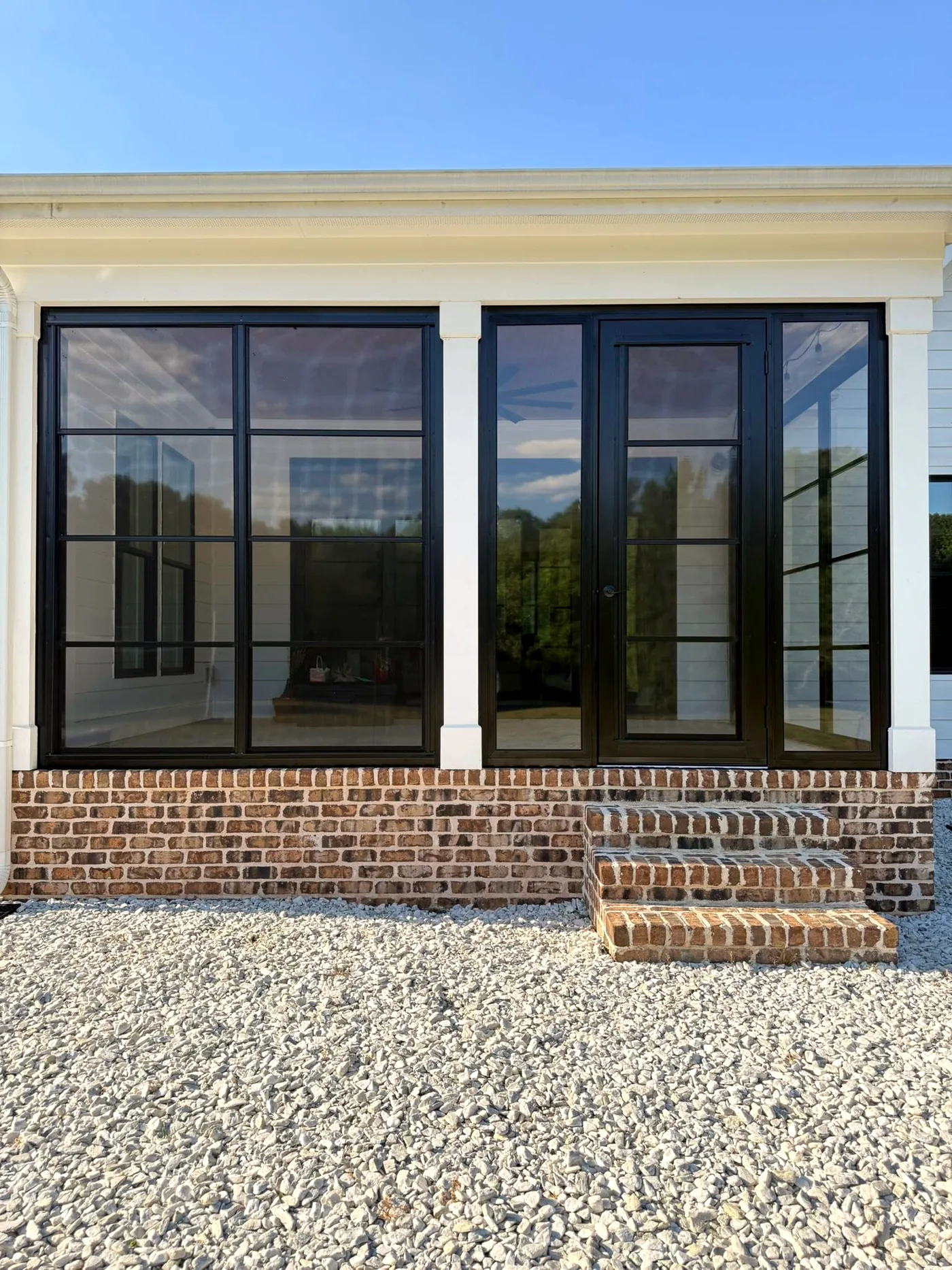 Three-season room with black-framed vinyl windows above a brick kneewall