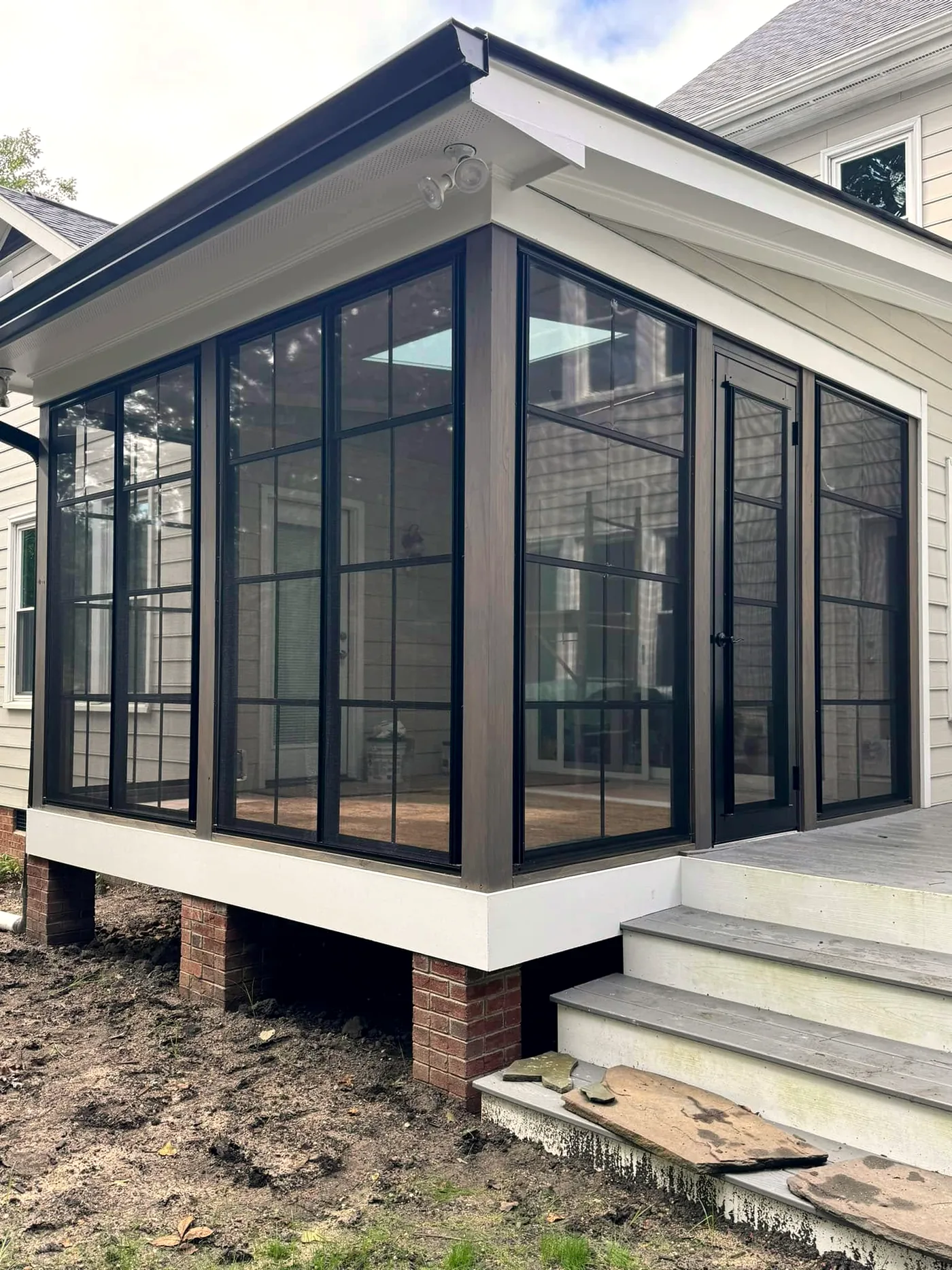 Corner three-season room with black-framed windows and a door opening onto a raised deck